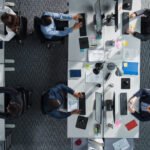 Top Down View of Diverse Colleagues Working In Corporate Office of Hedge Fund. Using Desktop Computers, Discussing Documents, Analyzing Data. Concept of Teamwork and Professional Business Environment