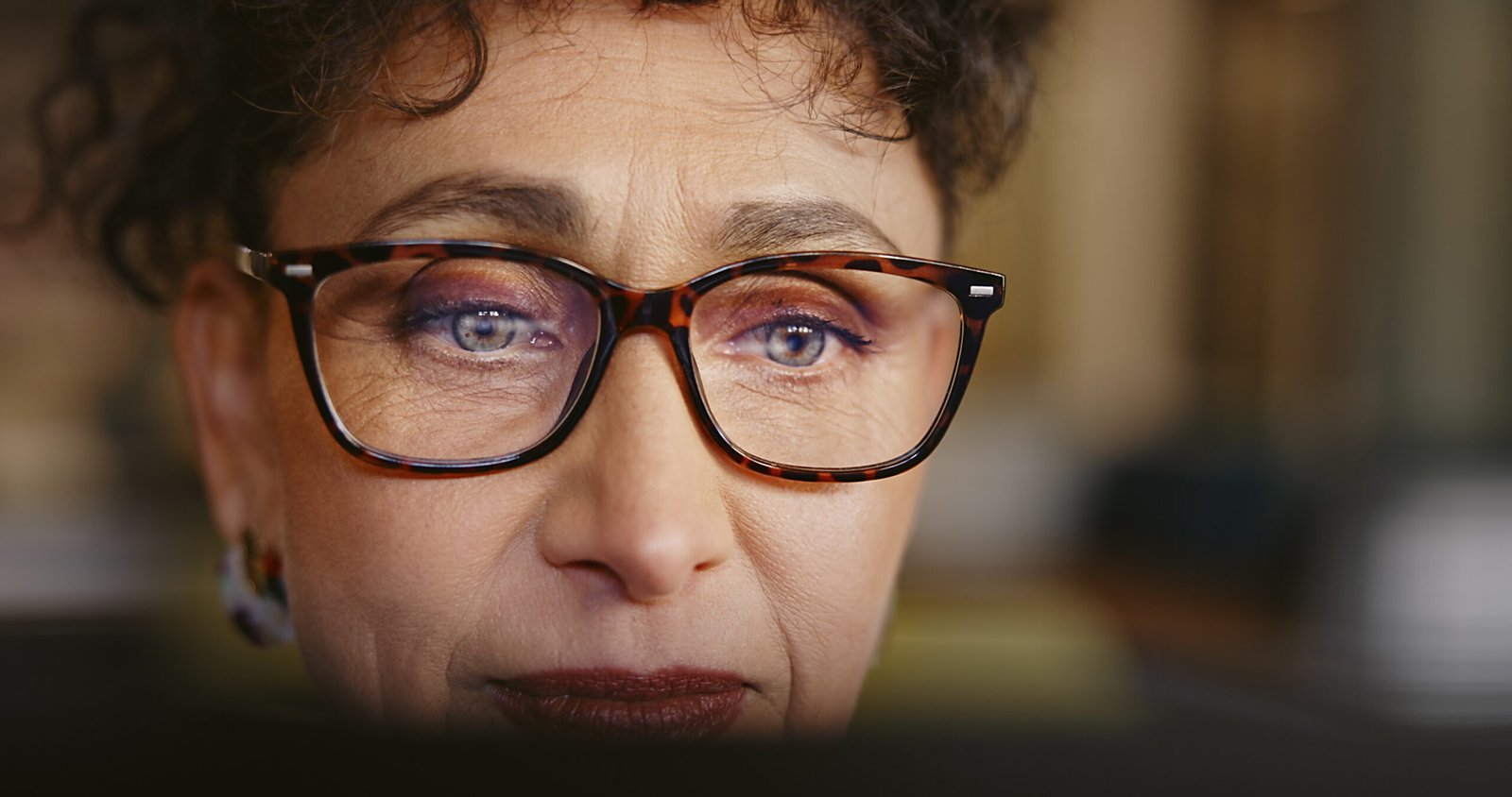 Face of business woman with reading glasses at computer for research, reflection and online analysis in office. Mature female employee working on website, internet and article at desktop screen